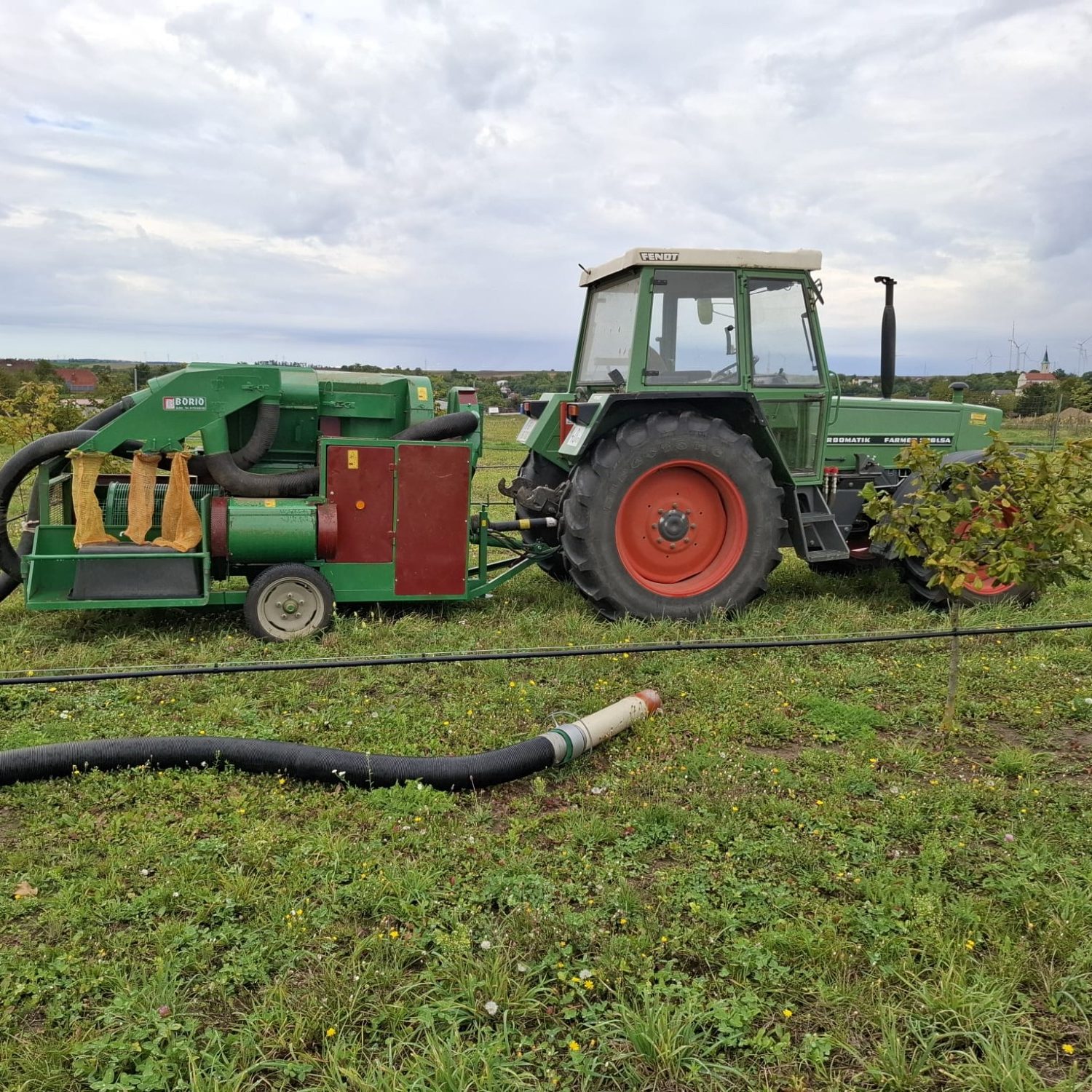 Traktor mit Erntemaschine auf einem Feld, umgeben von grüner Vegetation.