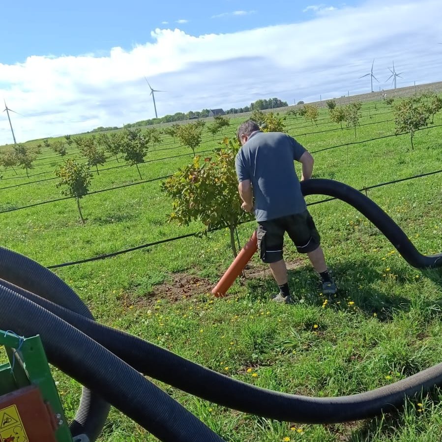 Ein Mann verwendet eine Maschine in einem Obstgarten zur Bewässerung oder Pflege.